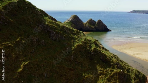 Aerial drone view flying over green cliffs onto a huge sandy beach at low tide Three Cliffs Bay, Gower, Wales photo