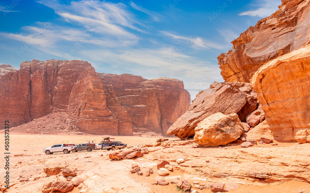 Red stones and rocks of Wadi Rum desert with jeeps in the background, Jordan