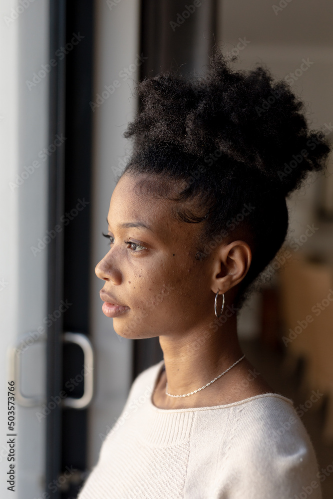 Close-up of serious thoughtful african american young woman looking through window at home Close-up of serious thoughtful african american young woman looking through window at home