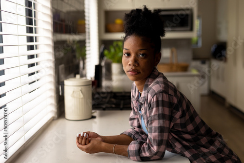 Portrait of serious african american young woman leaning on kitchen counter while standing at home