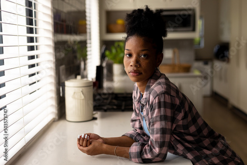 Portrait of serious african american young woman leaning on kitchen counter while standing at home photo