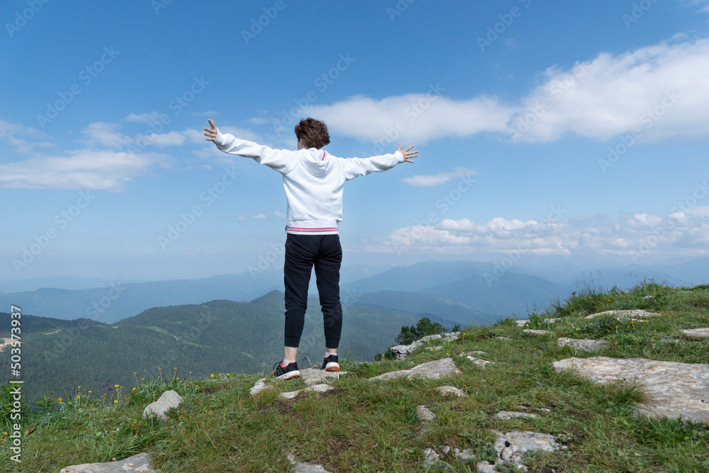Backview of girl with hands up standing on peak of mountains looking on blue sky and mountain landscape. Freedom and victory concept Backview of girl with hands up standing on peak of mountains looking on blue sky and mountain landscape. Freedom and victory concept