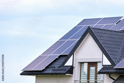 Residential house with rooftop covered with solar photovoltaic panels for producing of clean ecological electrical energy in suburban rural area. Concept of autonomous home