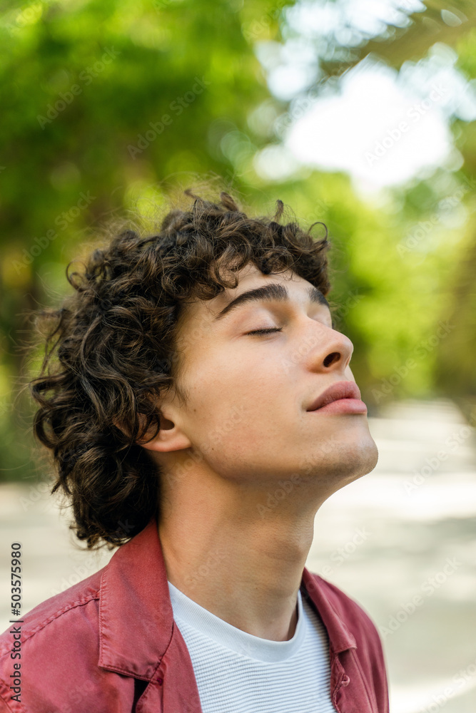 Relaxing young man standing with closed eyes and pleasure smile while walking outdoors Relaxing young man standing with closed eyes and pleasure smile while walking outdoors