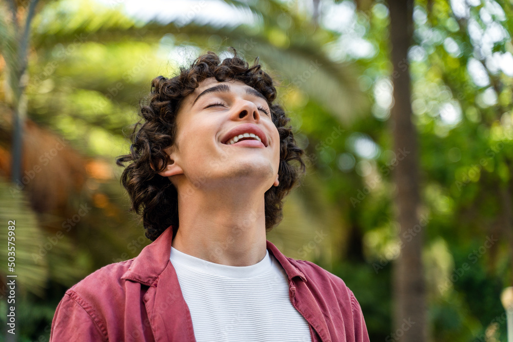 Happy caucasian curly man relaxing with closed eyes while standing at the street Happy caucasian curly man relaxing with closed eyes while standing at the street