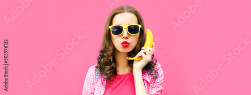 Colorful portrait of funny young woman calling on banana phone on pink background © rohappy