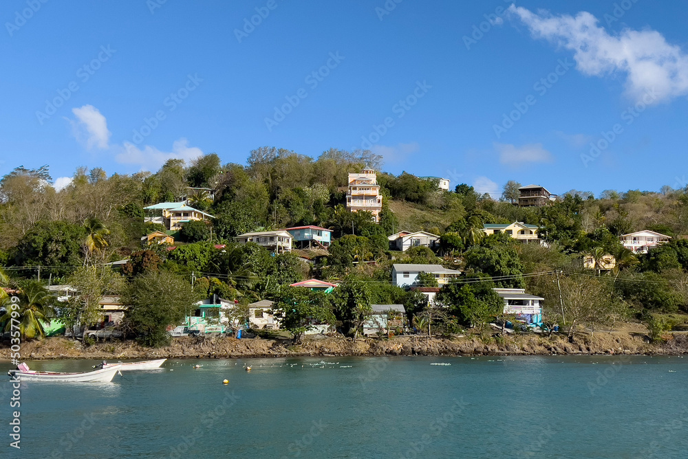 Houses of a fishing village on the island of saint Lucia nestled into a hillside overlooking the Caribbean Sea in evening sun with boats parked in the water near shore
