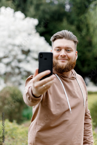 The guy cheerfully takes a selfie on the background of magnolia. Communicates via video call. shows the nature around him.