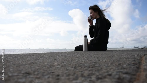 girl drinking tea from a thermos against the background of the sea. High quality FullHD footage