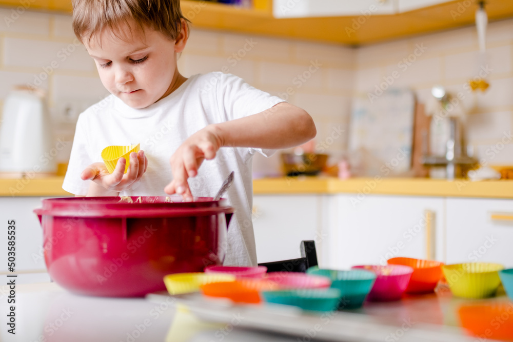 Little kid 5 years old cooks cupcakes in light kitchen at home. Little boy uses silicone baking molds Little kid 5 years old cooks cupcakes in light kitchen at home. Little boy uses silicone baking molds