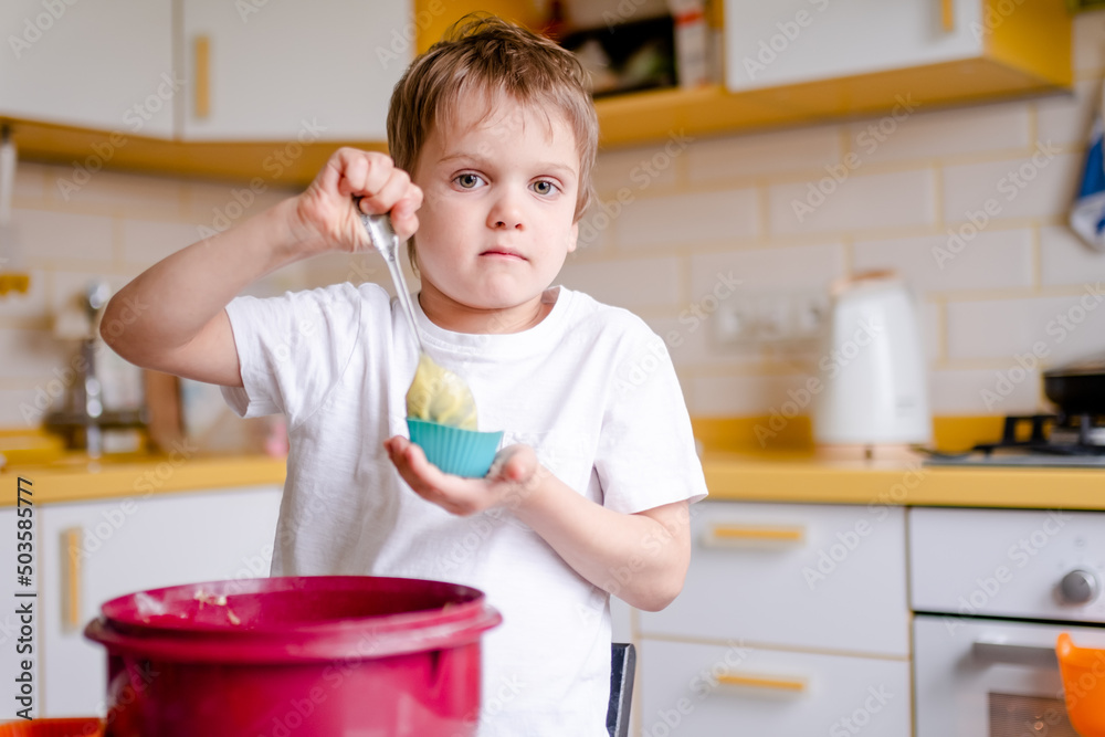 Little kid 5 years old cooks cupcakes in light kitchen at home. Little boy uses silicone baking molds Little kid 5 years old cooks cupcakes in light kitchen at home. Little boy uses silicone baking molds