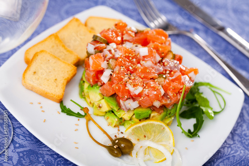 Popular dish of French cuisine is salmon tartar with avocado, served with a slice of lemon and croutons