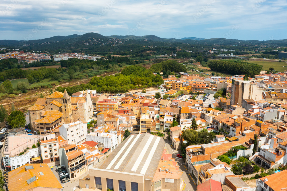 Scenic summer view of tiled roofs of residential houses of Spanish township of Tordera on background of greenery of Montnegre natural park on horizon on sunny day, province of Barcelona, Catalonia