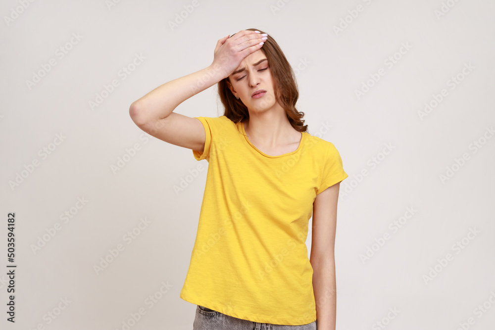 Portrait of upset beautiful female of young age in yellow T- shirt standing with facepalm gesture, blaming himself, feeling regret because of bad memory. Indoor studio shot isolated on gray background Portrait of upset beautiful female of young age in yellow T- shirt standing with facepalm gesture, blaming himself, feeling regret because of bad memory. Indoor studio shot isolated on gray background