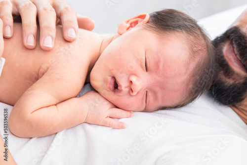 Close up of Asian newborn baby sleeping on his father's chest. Dad and son spend time together at home, young dad with cute little infant in his arms. Father and toddler in bed in the morning.