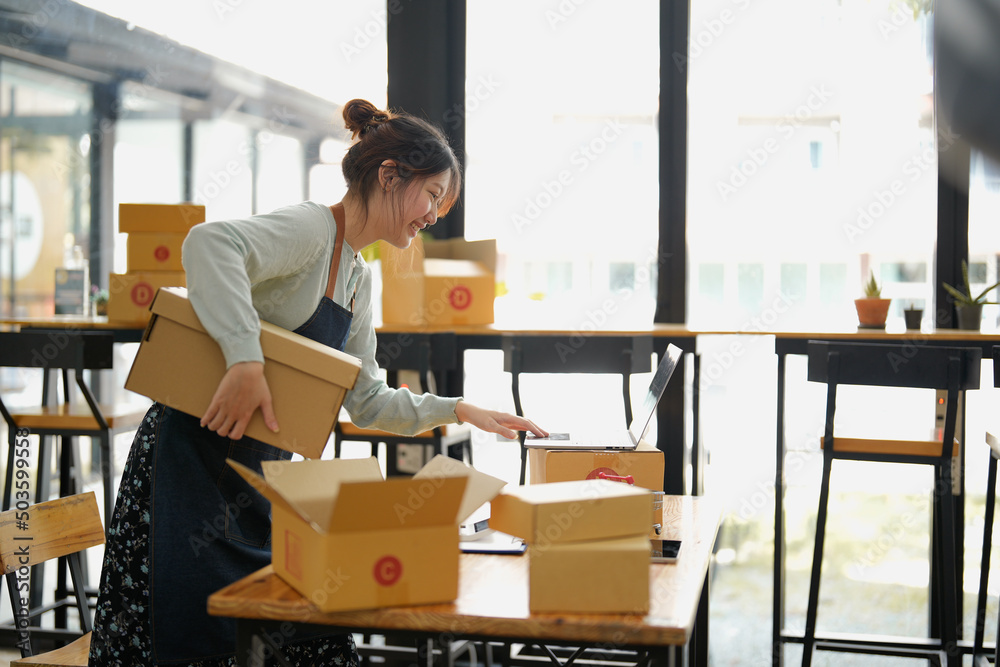 Startup small business SME, Entrepreneur owner using laptop computer taking receive and checking online purchase shopping order to preparing pack product box. Selling online ideas concept Startup small business SME, Entrepreneur owner using laptop computer taking receive and checking online purchase shopping order to preparing pack product box. Selling online ideas concept