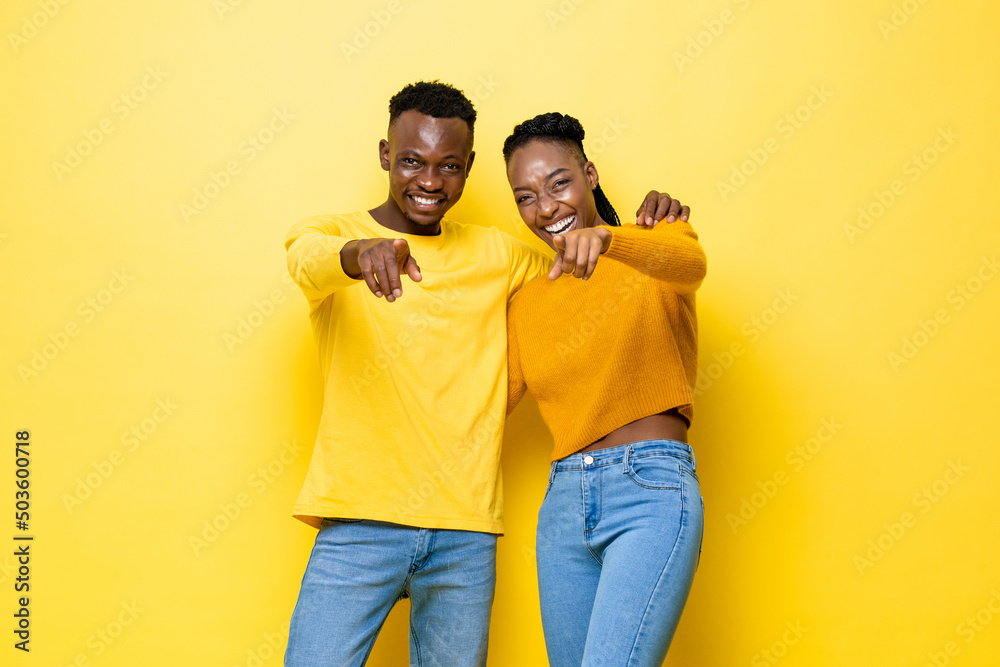Young happy African couple pointing at camera on isolated yellow stuido background Young happy African couple pointing at camera on isolated yellow stuido background