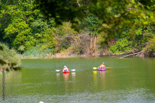 Beautiful view of friends kayaking in wild river near shore with green trees photo