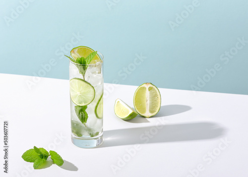 Ice and mojito in a glass lie on the table with a strong shadow