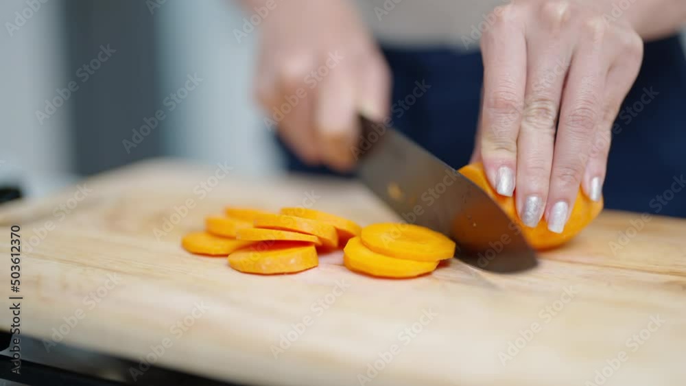 Close up of Asian woman hand using knife cutting fresh carrot on cutting board in the kitchen at home. Happy female enjoy cooking and having dinner eating healthy food on holiday vacation Close up of Asian woman hand using knife cutting fresh carrot on cutting board in the kitchen at home. Happy female enjoy cooking and having dinner eating healthy food on holiday vacation
