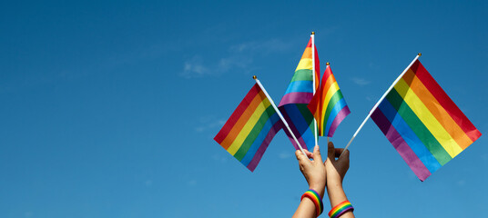 Rainbow flags showing in hands against clear bluesky, copy space, concept for calling all people to support and respcet the genger diversity, human rights and to celebrate lgbtq+ in pride month.