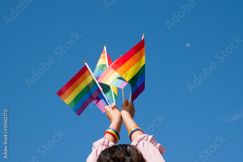 Rainbow flags showing in hands against clear bluesky, copy space, concept for calling all people to support and respcet the genger diversity, human rights and to celebrate lgbtq+ in pride month. photo