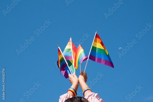 Rainbow flags showing in hands against clear bluesky, copy space, concept for calling all people to support and respcet the genger diversity, human rights and to celebrate lgbtq+ in pride month. photo