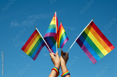 Rainbow flags showing in hands against clear bluesky  copy space  concept for calling all people to support and respcet the genger diversity  human rights and to celebrate lgbtq  in pride month.
