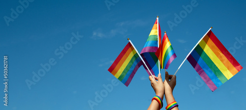 Rainbow flags showing in hands against clear bluesky, copy space, concept for calling all people to support and respcet the genger diversity, human rights and to celebrate lgbtq+ in pride month.