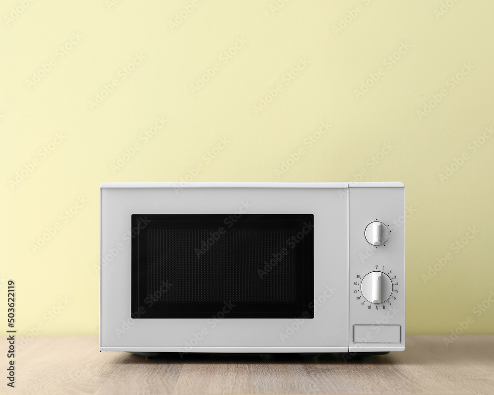 Obraz premium Microwave oven on wooden table against color background