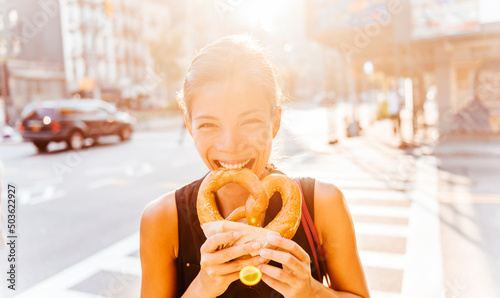 Woman eating pretzel in Manhattan, a classic New York City snack. Multiracial asian young professional portrait smiling at camera photo
