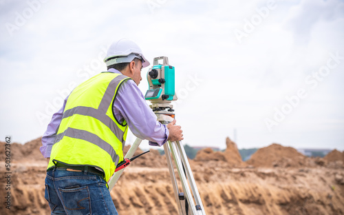 Surveyor engineer wearing safety uniform ,helmet and radio communication with equipment theodolite to measurement positioning on the construction site of the road with construct machinery background