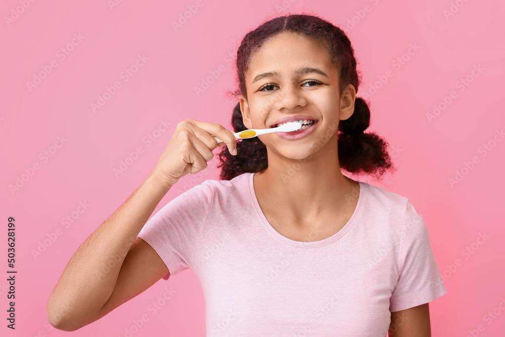 African-American teenage girl brushing teeth on pink background African-American teenage girl brushing teeth on pink background