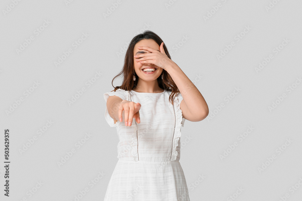 Young woman pointing at viewer on grey background Young woman pointing at viewer on grey background
