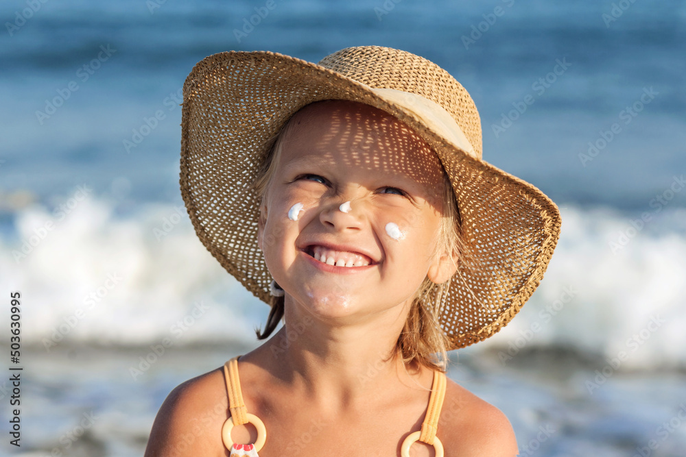 Sea Child Portrait. Child with Sunscreen on Face on Sea Waves Background. Happy Funny Kid Girl on Sea Beach. Summer Vacation on Sea and travel concept