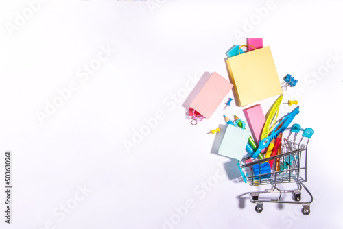 School sale concept. Shopping supermarket cart with colorful paper bags, school education supplies and accessories. Back to school shopping background, copy space