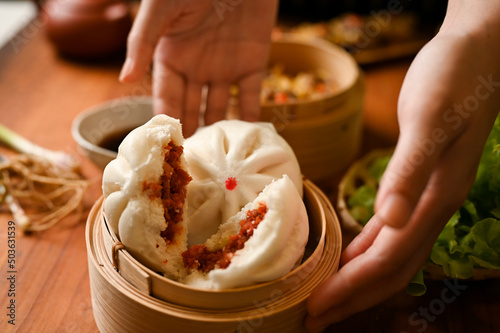 Female hands serving delicious steamed pork buns in a bamboo steamer