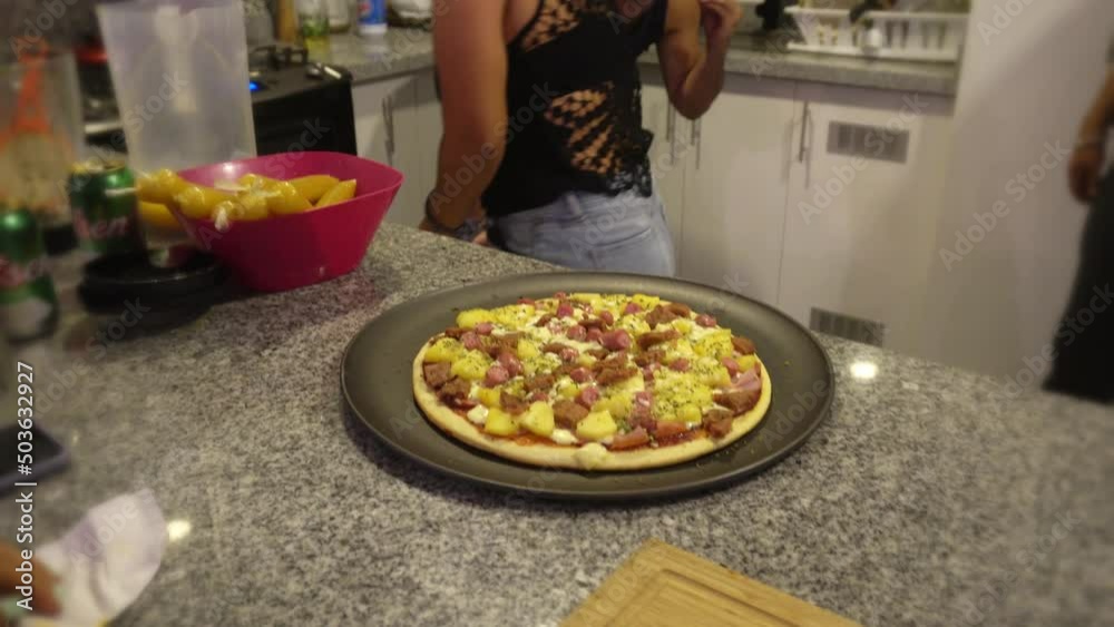 closeup taking a homemade pizza out of the oven in the kitchen between friends closeup taking a homemade pizza out of the oven in the kitchen between friends