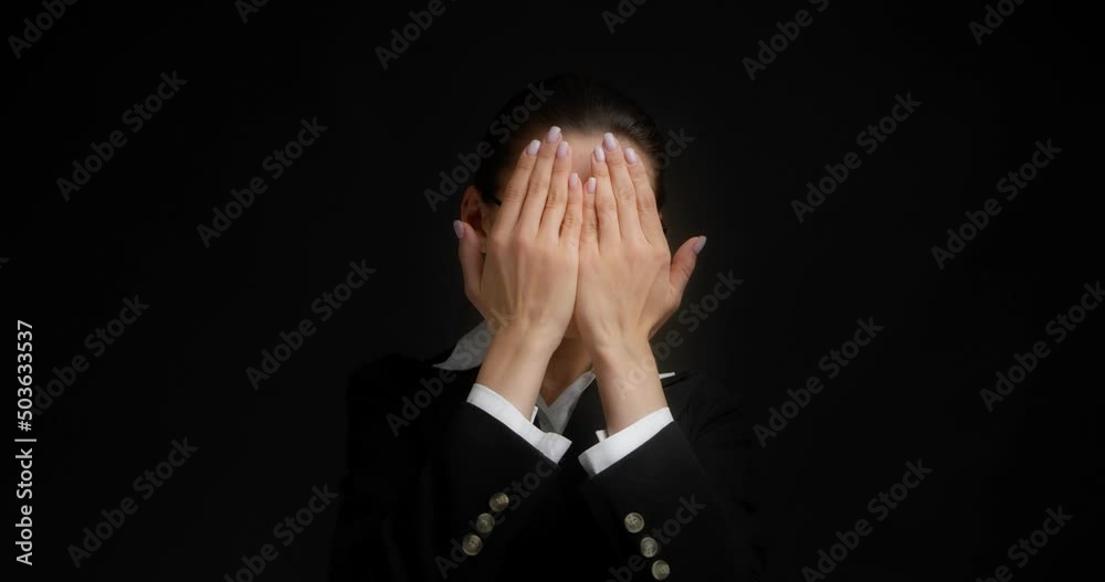 Business Asian woman with gathered hair is dressed in office clothes, covers her face with her palms, does not want to watch the news, do not show it. Isolated on a black background in the studio Business Asian woman with gathered hair is dressed in office clothes, covers her face with her palms, does not want to watch the news, do not show it. Isolated on a black background in the studio