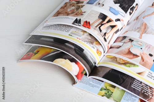 Many open magazines on white wooden table, above view