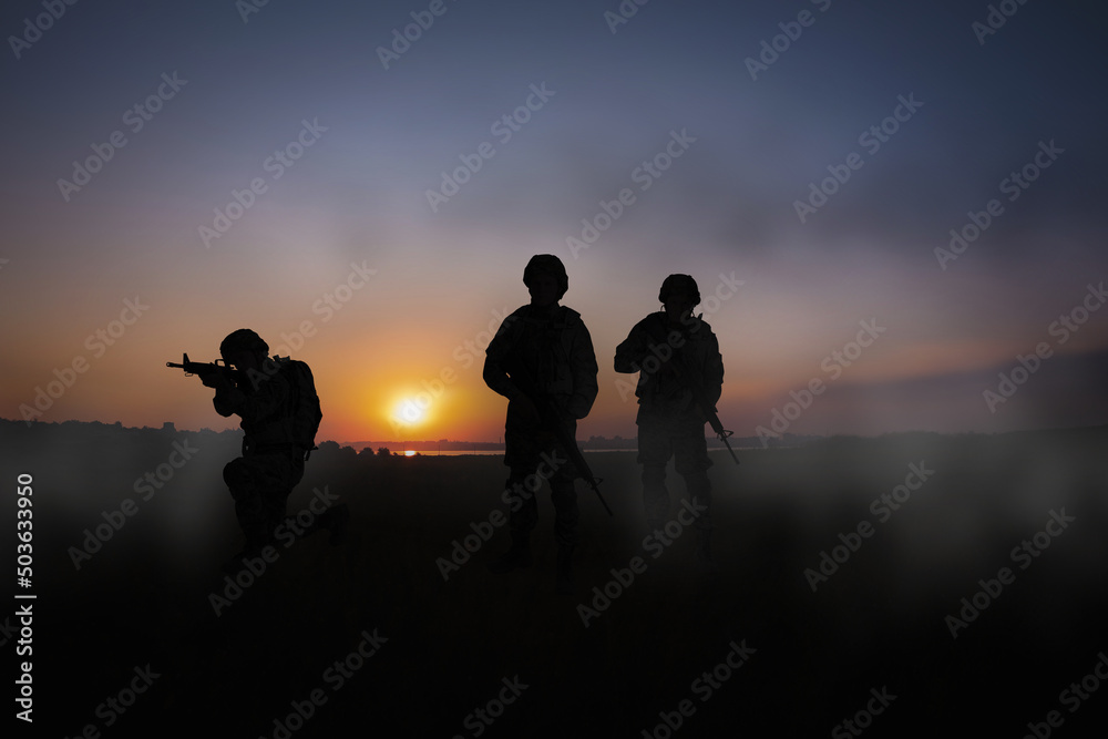Silhouettes of soldiers with machine guns on battlefield at sunset