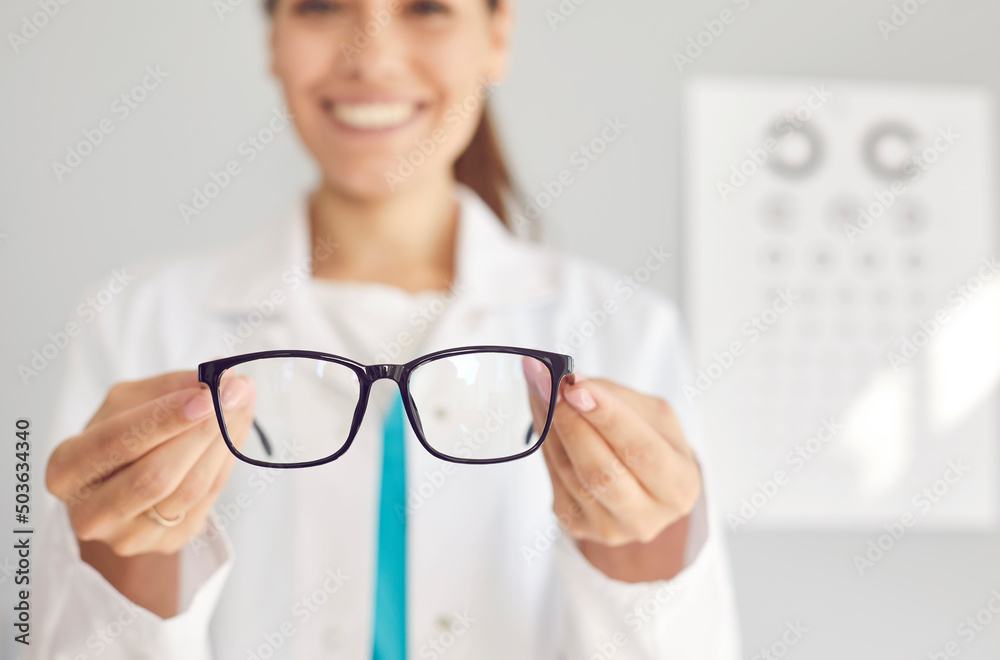 Close up of smiling woman optician offer glasses fir client or customer in optics salon. Female doctor recommend eyesight correction spectacles for good sight. Healthcare, medicine concept. - obrazy, fototapety, plakaty 