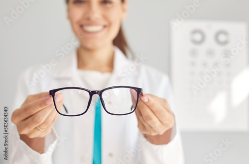 Close up of smiling woman optician offer glasses fir client or customer in optics salon. Female doctor recommend eyesight correction spectacles for good sight. Healthcare, medicine concept.