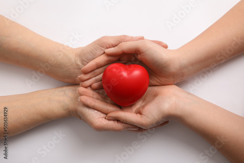 Young and elderly women holding red heart on white background  top view