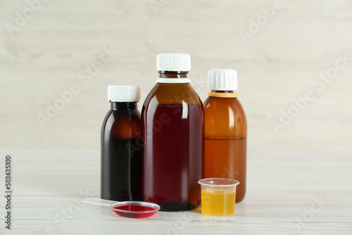 Fototapeta Naklejka Na Ścianę i Meble -  Bottles, spoon and measuring cup with cough syrup on white wooden table