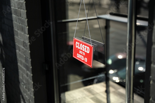 Red sign with text Closed Due To Covid-19 hanging on glass door. Coronavirus quarantine