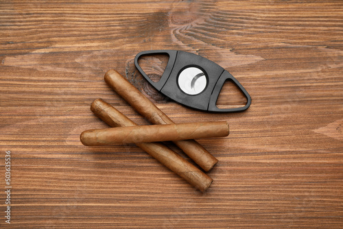 Cigars and guillotine cutter on wooden table, flat lay photo