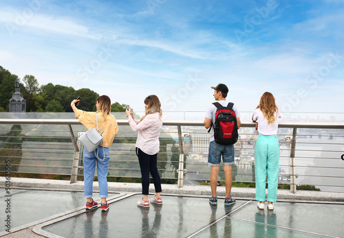 Young tourists on the glass bridge in Kyiv. View of the Dnieper river with rocks, green hills. Urban city life.