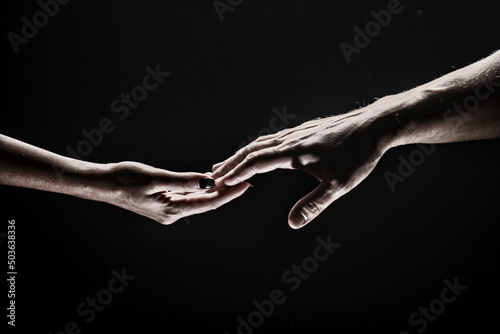 Two hands stretch each other, black background. Couple in love holding hads, close up. Helping hand, support, friendship.