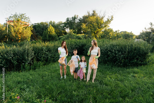 A group of adults and children together at sunset is engaged in garbage collection in the park. Environmental care, waste recycling. Sorting garbage.